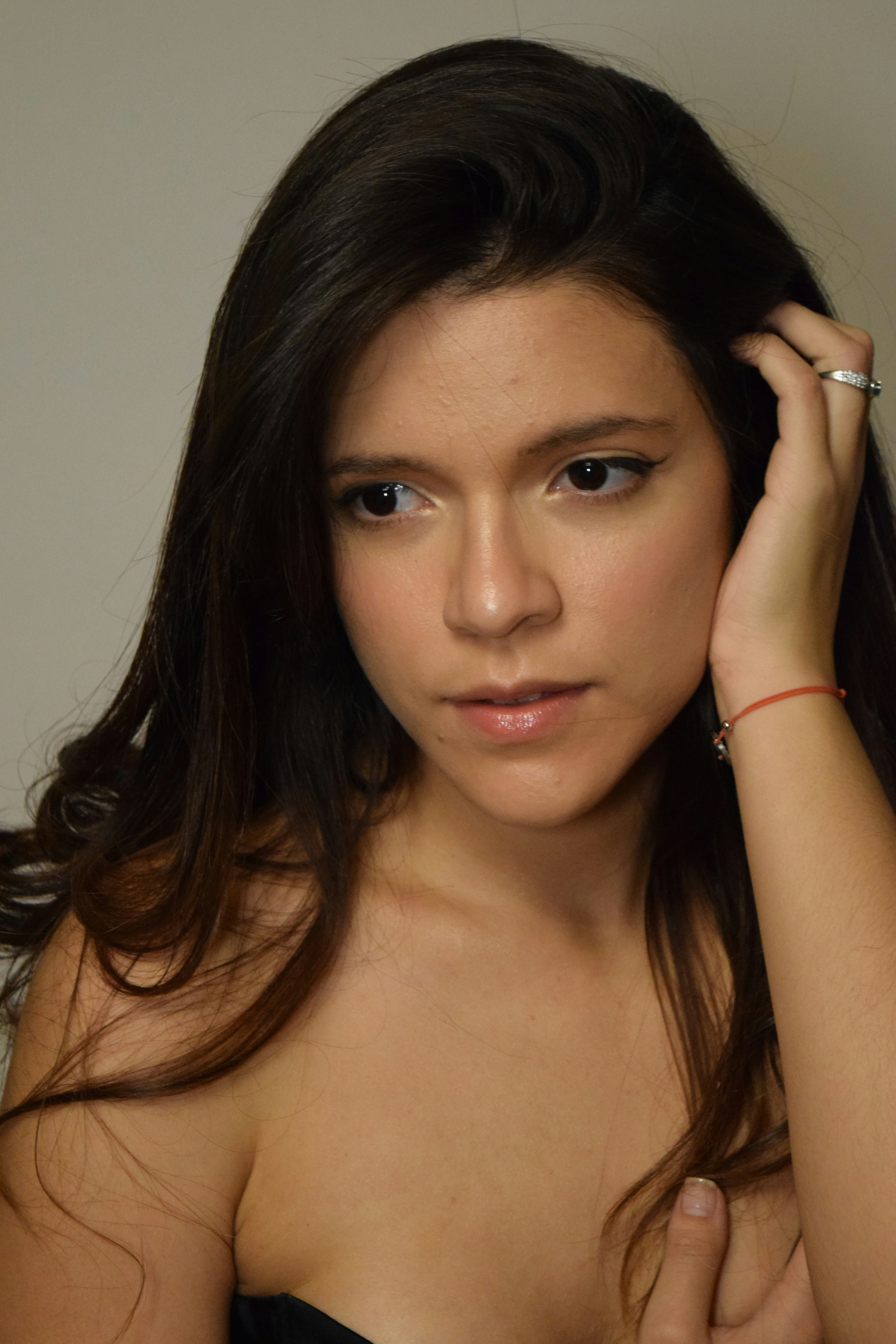 Woman with long brown hair wearing a black strapless top and red bracelet in 2025