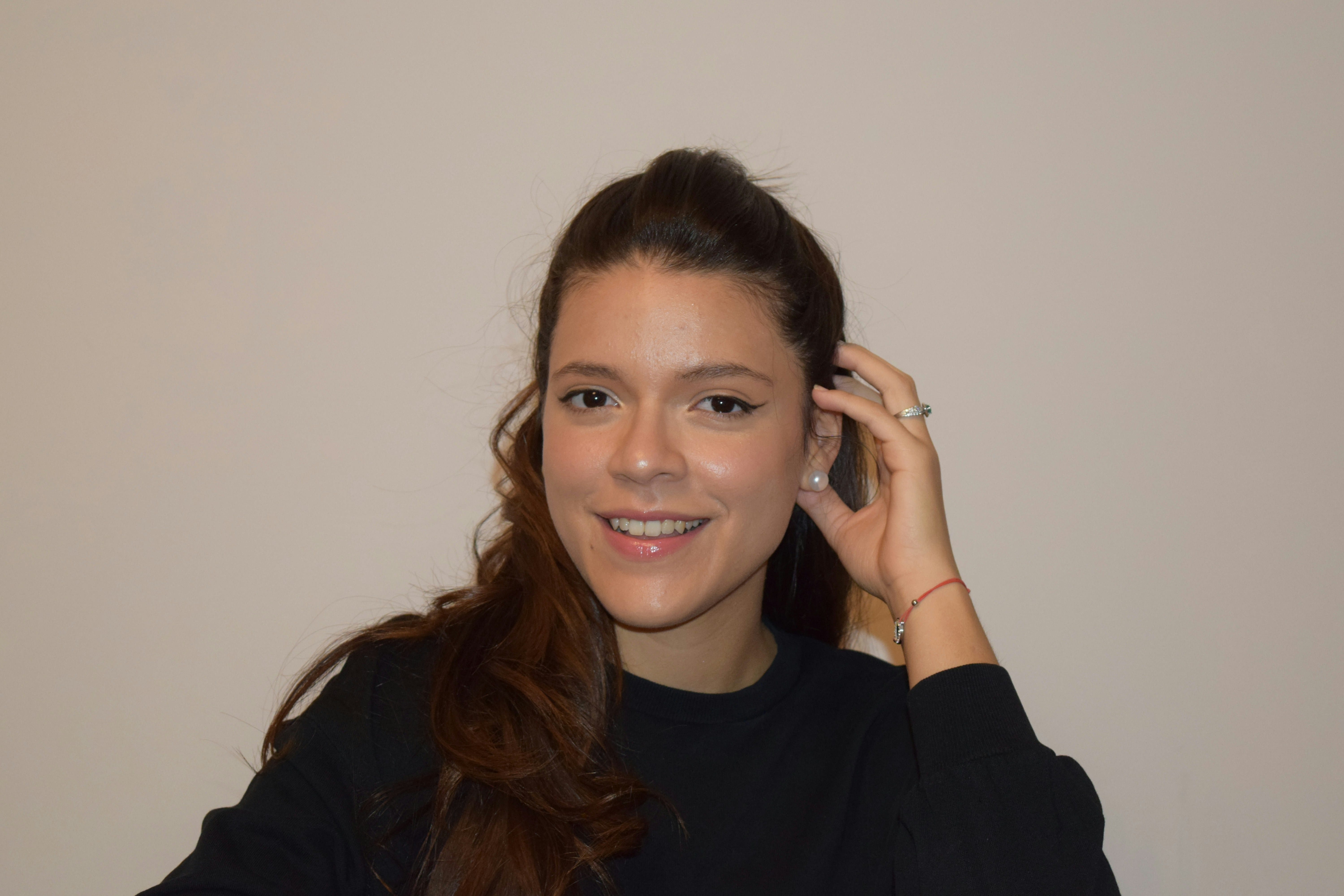 Woman with a high ponytail wearing a black long-sleeve top, pearl earrings, and a red bracelet in 2025