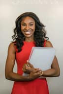 Smiling woman wearing a red dress, holding a folder, standing in front of a neutral background.