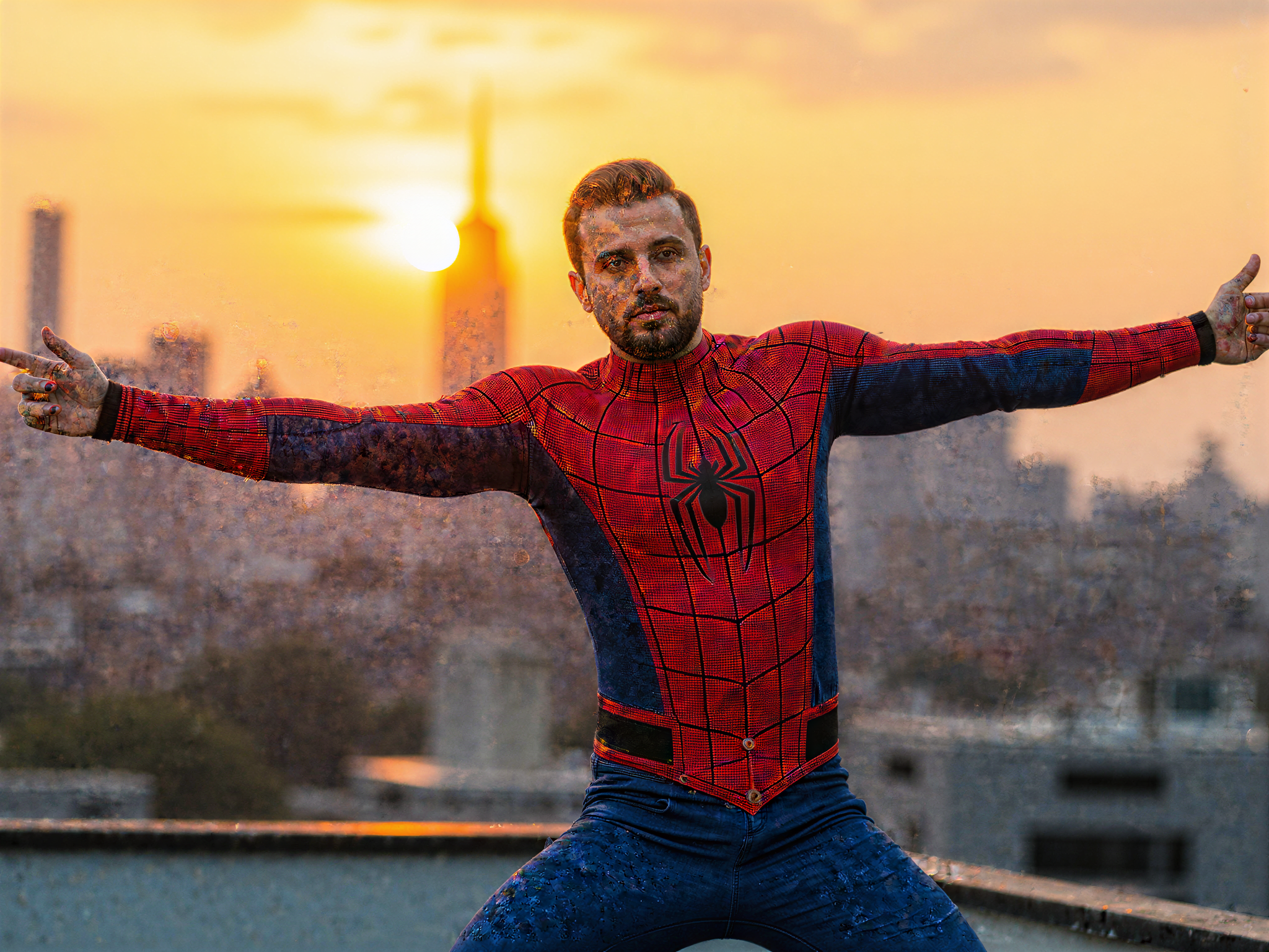 A 32-year-old man, OD62S, embodying the cheerful spirit of Spider-Man in a hyper-realistic portrayal. He wears a meticulously crafted Spider-Man suit featuring the iconic red and blue design, complete with web patterns. His mask is pulled back to reveal a joyful expression, showcasing his bright smile and twinkling eyes filled with enthusiasm. The urban backdrop features a vibrant New York City skyline, hinting at the character's adventurous life, with the sun setting in the background to create a warm, golden hour glow. He stands in a dynamic pose on a rooftop, arms extended as if ready to swing into action, embracing the thrill of being a superhero. The entire scene exudes a sense of happiness and freedom, capturing the essence of heroism in a playful manner.