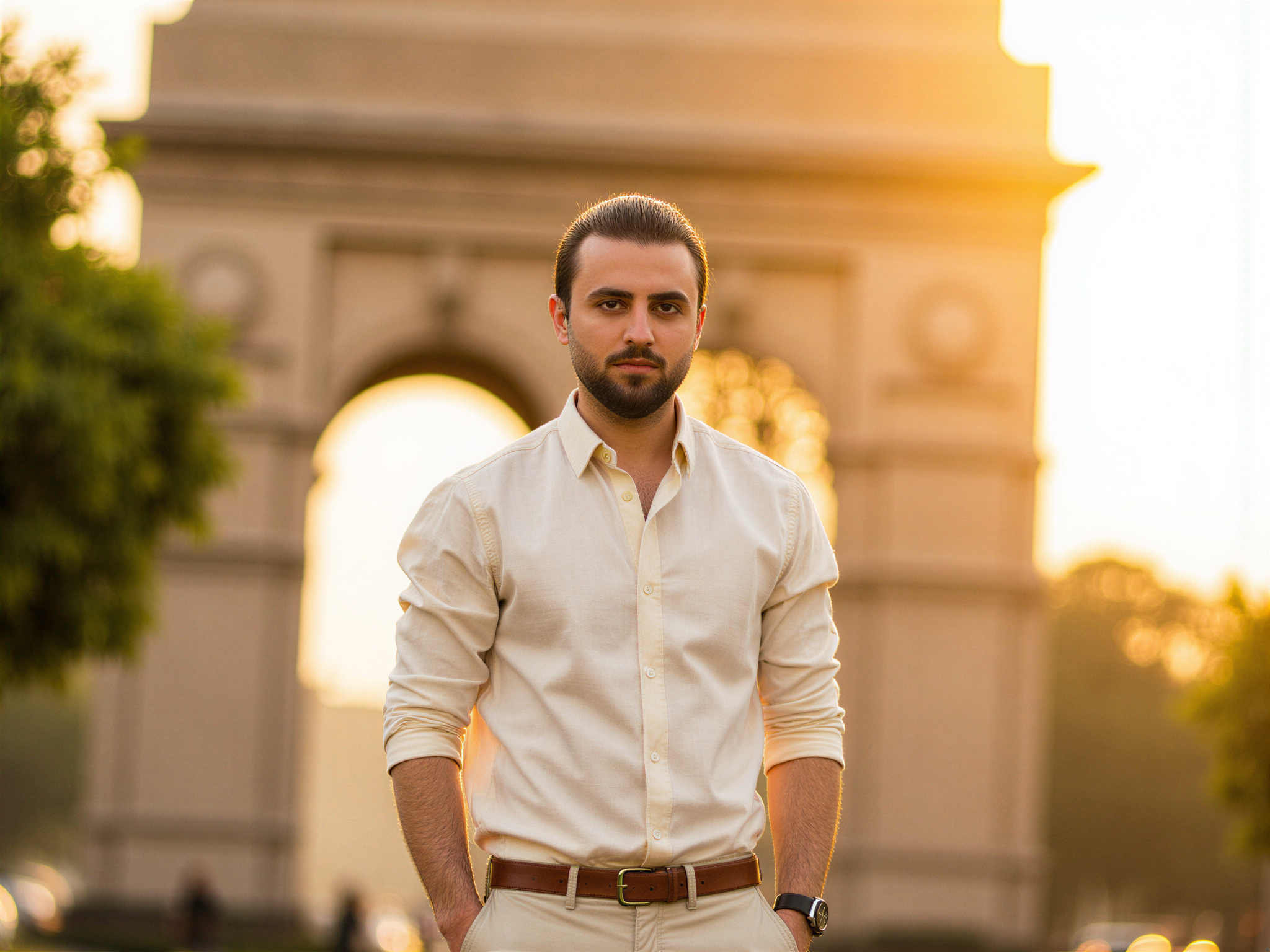 A joyful male figure, OD62S, aged 32, stands in front of the majestic India Gate in New Delhi, embodying a sense of pride and happiness. He is dressed in a tailored linen shirt in soft ivory and fitted chinos, effortlessly blending elegance with casual charm. The warm golden hour light bathes him, flattering his features and creating a glow on the polished stone of the monument behind him. He flashes a radiant smile, his eyes sparkling with joy as he captures the essence of celebration in this iconic setting. The composition highlights the grandeur of India Gate, framed by lush greenery, invoking a sense of cultural pride and connection to heritage, while the mood is unmistakably cheerful and vibrant.