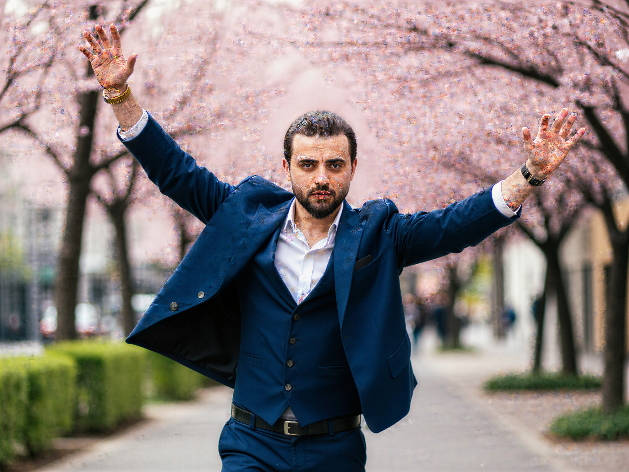 A joyful male figure, OD62S, aged 32, embodying the spirit of Japan in a vibrant urban setting. He wears a contemporary kimono-inspired jacket in a rich indigo hue, layered over tailored trousers. The scene captures him against a backdrop of cherry blossom trees in full bloom, their delicate petals gently falling around him, adding to the cheerful atmosphere. His expression beams with happiness as he extends his arms, inviting the viewer into his joy. Soft, natural lighting bathes the scene, highlighting the colors and textures of his attire and the serene beauty of the surroundings. The composition balances dynamic motion with a sense of tranquility, celebrating the cultural richness of Japan through an uplifting lens.