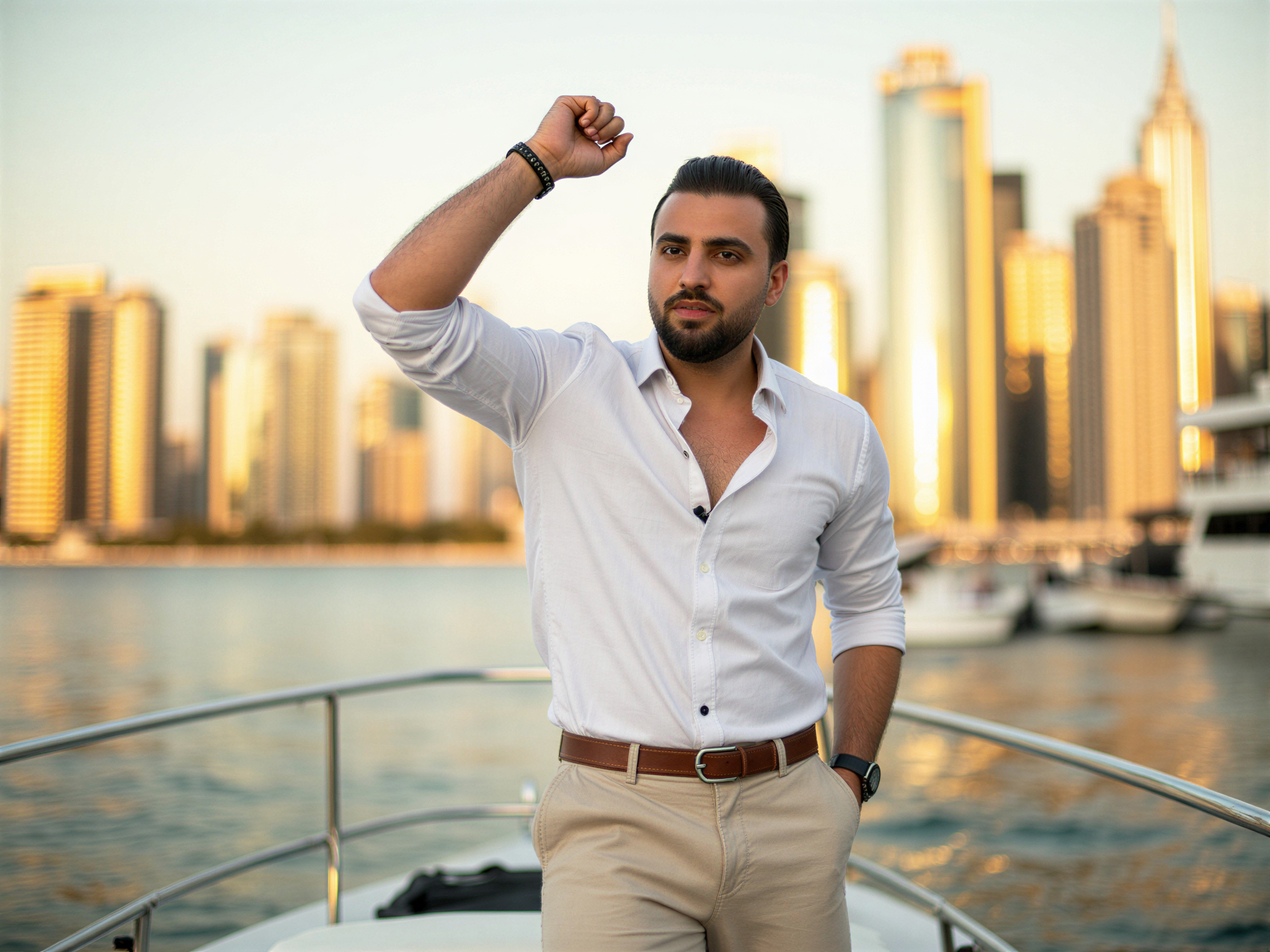 A charismatic male figure, OD62S, aged 32, captured in the vibrant setting of Dubai Marina. He exudes joy as he stands confidently on a sleek yacht, the stunning skyline of modern architecture shimmering in the background. Dressed in a tailored white linen shirt and light beige chinos, his casual elegance complements the sun-kissed atmosphere. The soft golden hour light casts a warm glow on his face, accentuating his broad smile and sparkling eyes. With one arm raised in elation, the pose captures a moment of pure happiness and celebration, embodying the lavish lifestyle of Dubai without overshadowing the breathtaking cityscape behind him. The composition utilizes the rule of thirds, drawing the viewer's eye from the subject to the vibrant surroundings, creating a harmonious blend of emotion and luxury.