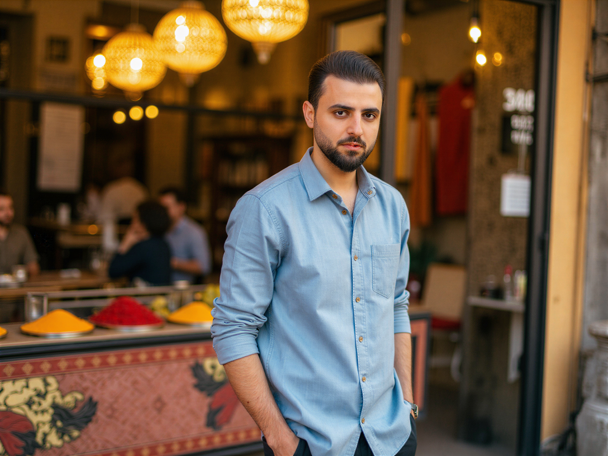 A charismatic male subject, OD62S, aged 32, captured in a vibrant street scene in Sharjah, radiating happiness. He wears a lightweight linen shirt in a soft azure, perfectly complementing the warm hues of the surrounding architecture. The atmosphere is filled with the dynamic energy of the bustling marketplace, with colorful textiles and spices surrounding him. He stands amidst intricate Islamic architecture, with playful sunlight enhancing the textures of the scene. His pose is relaxed, hands casually in his pockets, exuding an aura of joy and contentment. The composition utilizes natural lighting to create soft shadows, while the lively backdrop tells a rich cultural story.